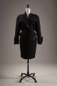 Black suit of fitted jacket with peplum, asymmetrical collar and cuffs and faux leather trim an…