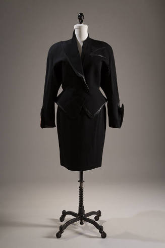 Black suit of fitted jacket with peplum, asymmetrical collar and cuffs and faux leather trim an…