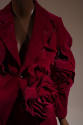 Detail view of red suit jacket showing notched lapel, oversize dimensional floral shapes and sl…