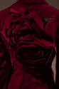 Back view of red suit jacket showing slashes in fabric and oversize dimensional floral shapes a…