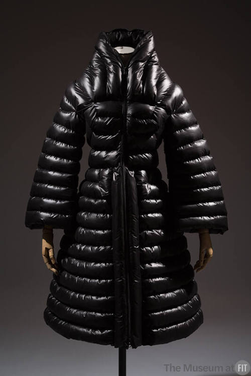 Black puffer coat with horizontal quilting, stand collar, bell sleeves, fitted waist and flared…