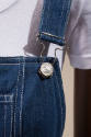 Detail view of dark blue denim overalls dress showing front buckle fastening with smiling face …
