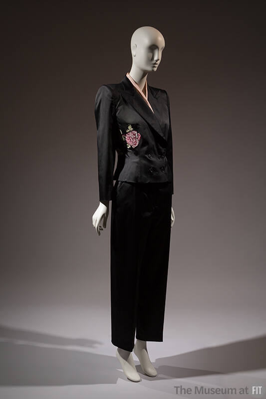 ¾ view of black evening pantsuit with double breasted jacket with pink rose embroidered at left…