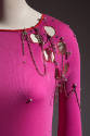 Detail view of hot pink evening top showing circular cut outs, safety pin, draped silver chain …