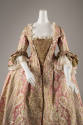 Detail view of pink robe a la francaise gown showing green lace bodice panel, white lace trim a…