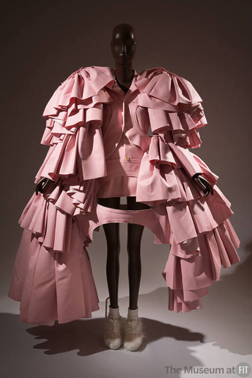 Pink harness with oversize layered sleeves of gathered flounces reaching to floor over matching…