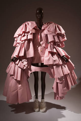 Pink harness with oversize layered sleeves of gathered flounces reaching to floor over matching…
