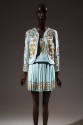 Light blue suit with allover gold tone studs in spiral patters on collarless jacket and Greek k…