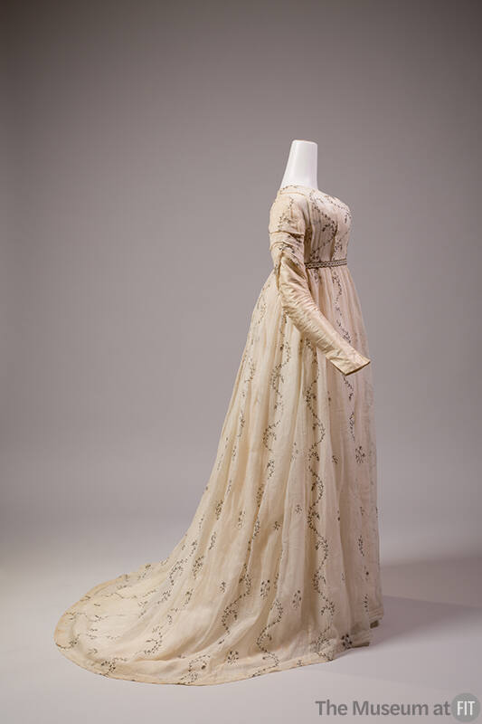 Side view of white muslin long sleeve dress with allover embroidered vines and floral springs, …