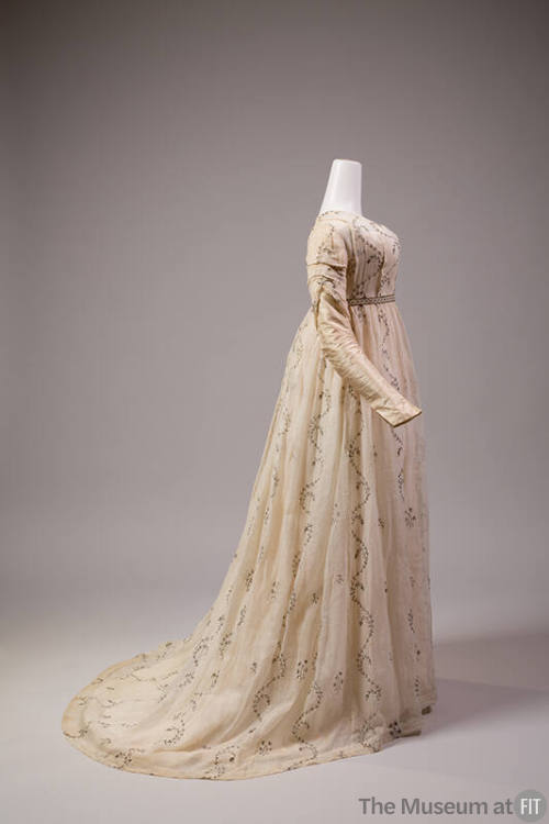 Side view of white muslin long sleeve dress with allover embroidered vines and floral springs, …