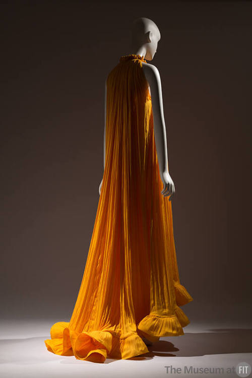 Back view of pleated dark yellow floor length halter dress with ruffled high neckline and ruffl…