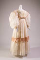 White organdy floor length dress with balloon sleeves, pink trim on collar that extends over bo…