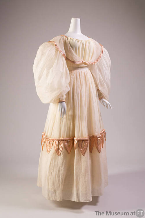White organdy floor length dress with balloon sleeves, pink trim on collar that extends over bo…