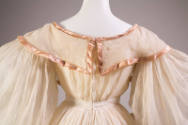 Back view of white organdy dress bodice showing pink trim on foldover collar and shirred balloo…