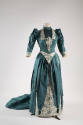 Blue green two-piece floor length dress with puffed sleeves, white and blue green brocade trim …