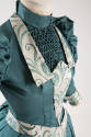 Detail view of blue green dress bodice showing band collar, smocked plastron and white trim wit…