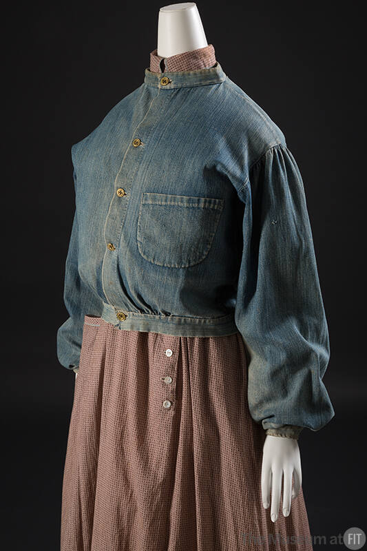 ¾ view of blue denim button front jacket with band collar, right patch pocket and loose sleeves…