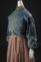 ¾ view of blue denim button front jacket with band collar, right patch pocket and loose sleeves…
