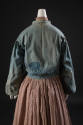 Back view of blue denim jacket showing reverse applique patches on lower sleeves and on left lo…