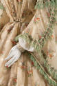 Detail view of beige floral print dress showing green fringe trim on bell sleeves and large sca…