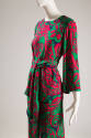 ¾ view of green, pink, red, purple, paisley print ensemble showing bell sleeves and scarf tied …