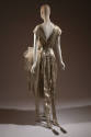 Back view of silver lamé cap sleeve v-back dress with embroidered net layered skirt, two long b…