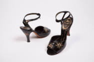 Pair of black high heel ankle strap sandals with painted flowers throughout and gold Delman log…