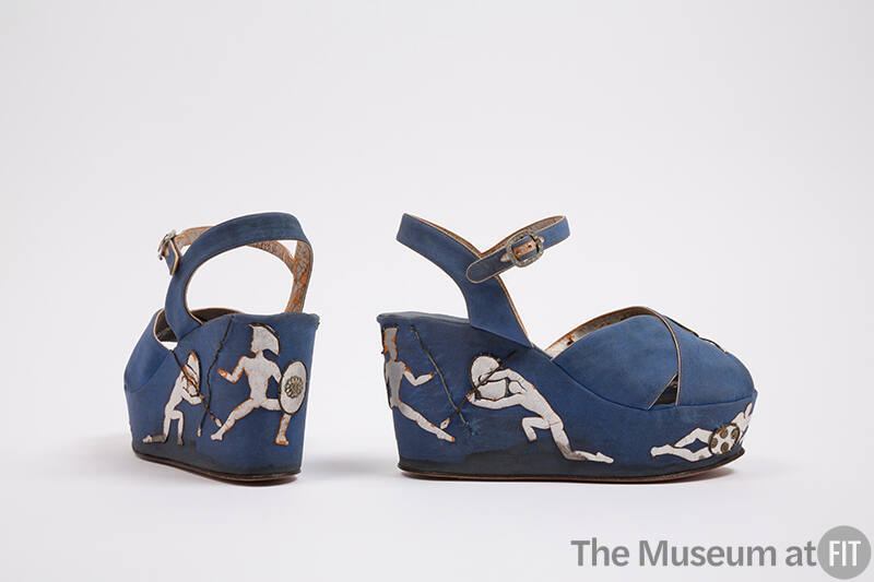 Pair of blue wedge sandals with silver metallic piping, appliqué warrior figures on the platfor…