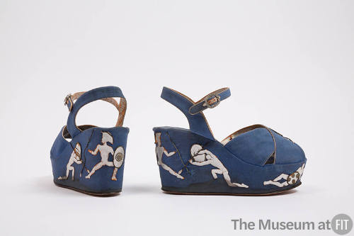 Pair of blue wedge sandals with silver metallic piping, appliqué warrior figures on the platfor…