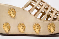 Side view of off-white platform sandals with latticework vamp and gold metal cherub heads on pl…