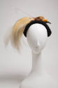 Small black hat with rolled brim and trimmed with bird of paradise with large cream tail feathe…