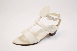 White T strap sandals with T extending to ankle strap with large round center circle, black lea…