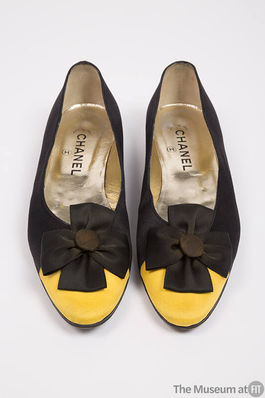Pair of black flat shoes with yellow toe cap, black cockade at vamp and Chanel brand name visib…