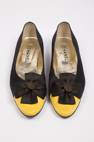Pair of black flat shoes with yellow toe cap, black cockade at vamp and Chanel brand name visib…