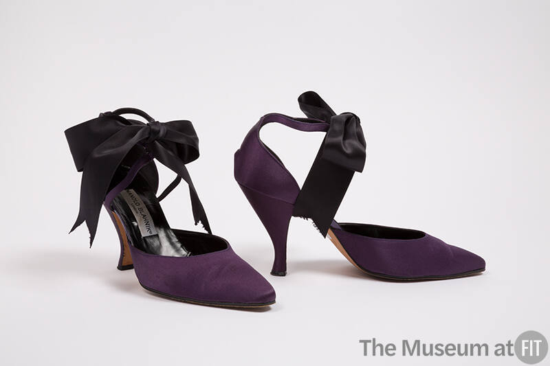Pair of purple d'Orsay shoes with high heels and large black satin bow at ankle strap