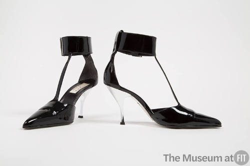Black T strap shoes with pointed toe, wide buckled ankle strap, and silver high heel
