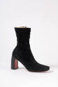 View of single black ankle boot with curved heel and red sole
