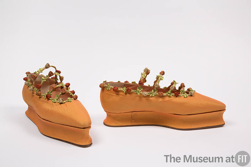 Pair of orange flat shoes with platform sole, pointed toe and trimmed around topline and four n…