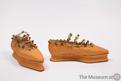 Pair of orange flat shoes with platform sole, pointed toe and trimmed around topline and four n…