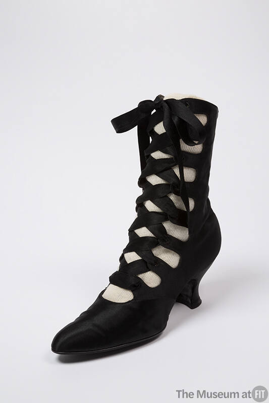Black calf height boot with crisscrossing lace up front closure, slightly rounded pointed toe a…