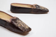 Detail view of dark purple/brown leather slippers showing light purple floral cutout design at …