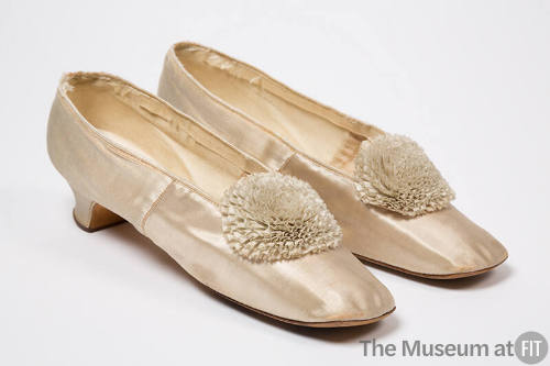 Pair of ivory court style shoes with large pleated rosette pom poms at top center, square toe a…