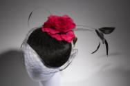 Overhead view of black velvet skull cap showing black face veil, large red rose and green leave…