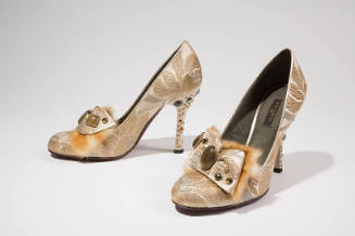 Ivory high heel pumps with metallic gold and grey floral pattern; attached beaded bow ornament 