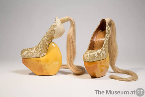 gold metallic lace over beige heel-less shoes with high wood platform and blond hair ponytail a…