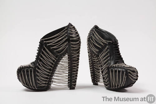 Black high heel platform lace up shoes with silver metal chains in a corset-like lacing web des…