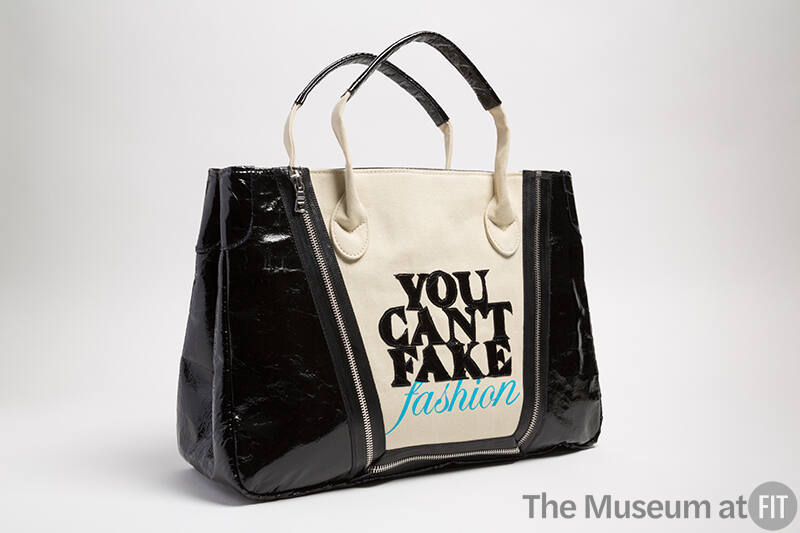 Dark beige tote bag with black sides and black appliqued letters "YOU CAN'T FAKE FASHION" 