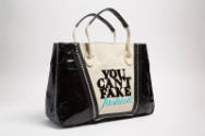 Dark beige tote bag with black sides and black appliqued letters "YOU CAN'T FAKE FASHION" 