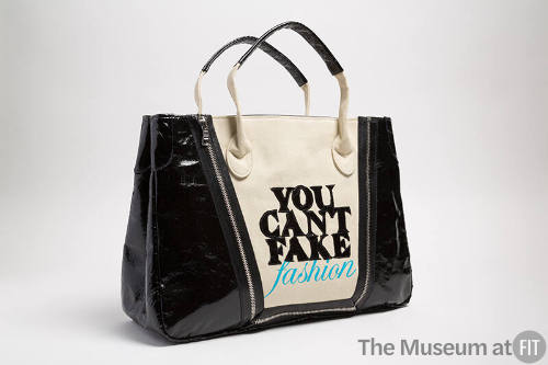 Dark beige tote bag with black sides and black appliqued letters "YOU CAN'T FAKE FASHION" 