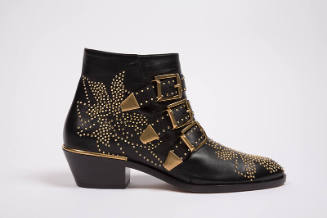 Black low heeled ankle boot with allover gold metal studs in a flower motif and three large gol…